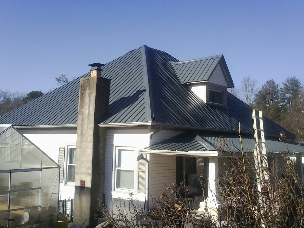 Dark blue standing seam metal roof on a white farmhouse with dormer — Slate & Tile Roof Repair by Roofing Brothers in Wise River