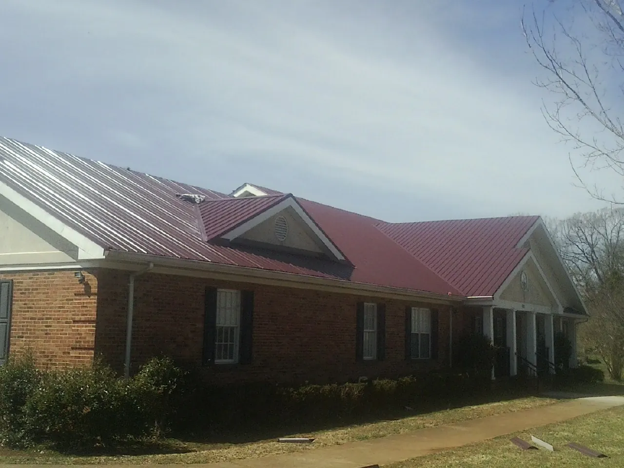 Red metal roof with gabled entries on a long brick building, from a Hail Damage Roof Repair job in Wise River