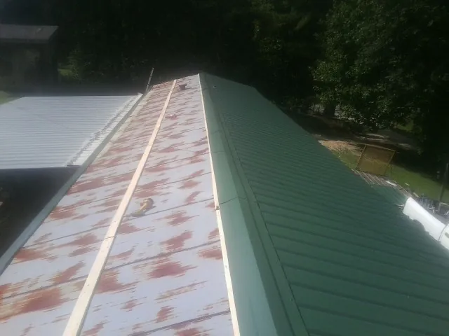 Old rusted panels beside newly installed green metal roofing — Wind Damage Roof Repair by Roofing Brothers in Wise River