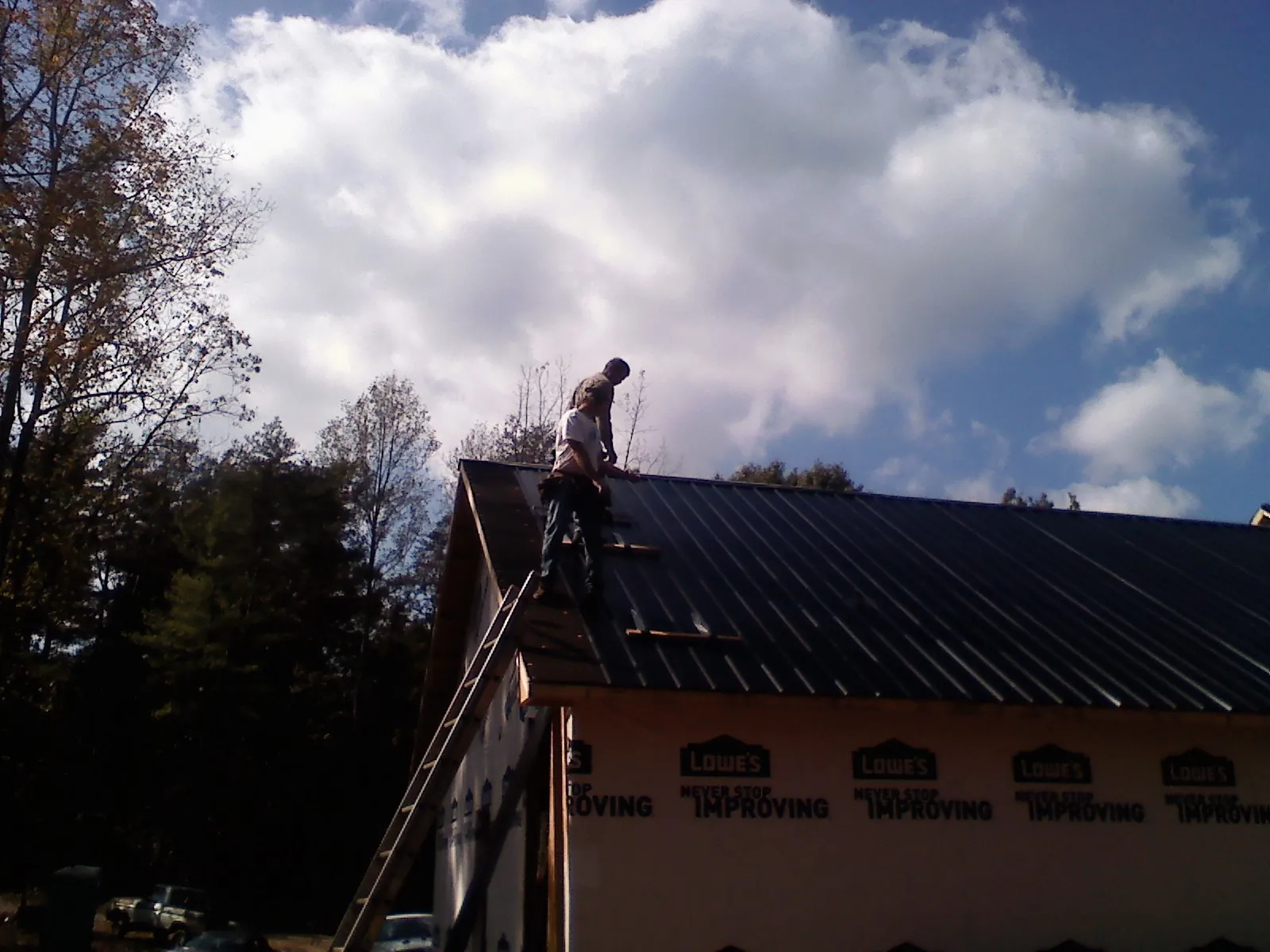 Roofer fastening dark metal panels high against a cloudy sky, from a Roof Inspection job in Wise River