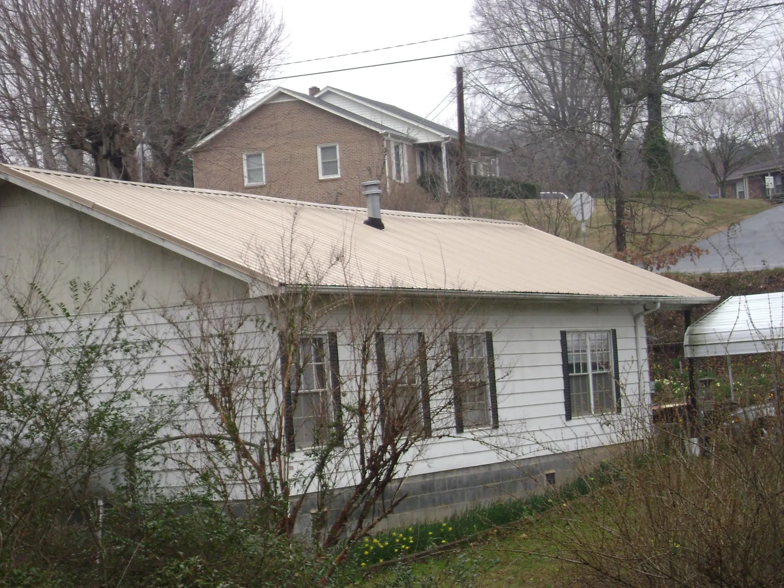 Tan metal roof on a white sided house set into a hillside — Commercial Roofing by Roofing Brothers in Wise River